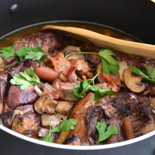 Coq au Vin in a Dutch oven – French braised chicken in red wine with bacon, mushrooms, and pearl onions.