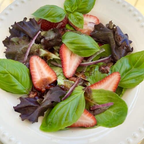 Fresh strawberry basil salad with romaine lettuce, red onion, and a strawberry balsamic vinaigrette served in a white bowl.